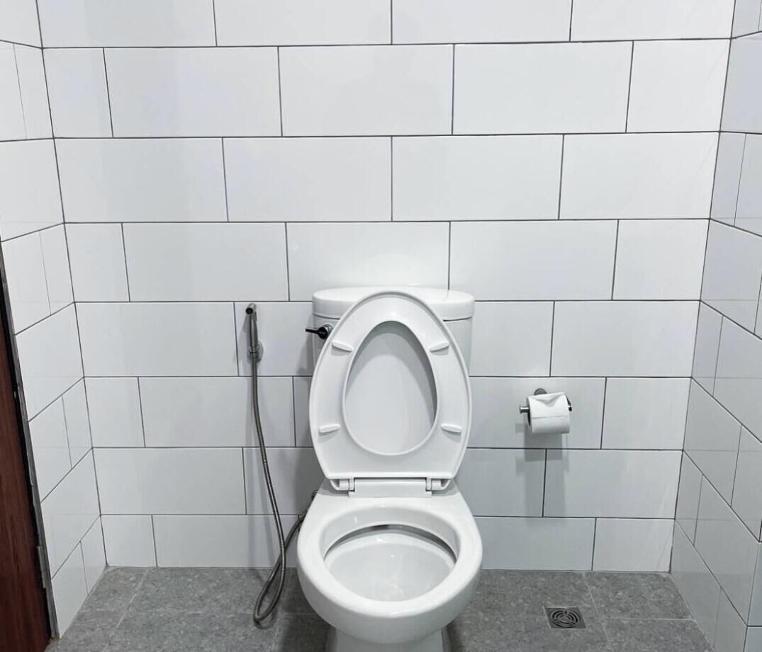 Ein kleines, sauberes Badezimmer mit weißen Fliesen, einer weißen Toilette und einer Dusche.