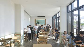 Un amplio comedor interior con techos altos y ventanas grandes, con mesas y sillas de madera, y un ventilador central.