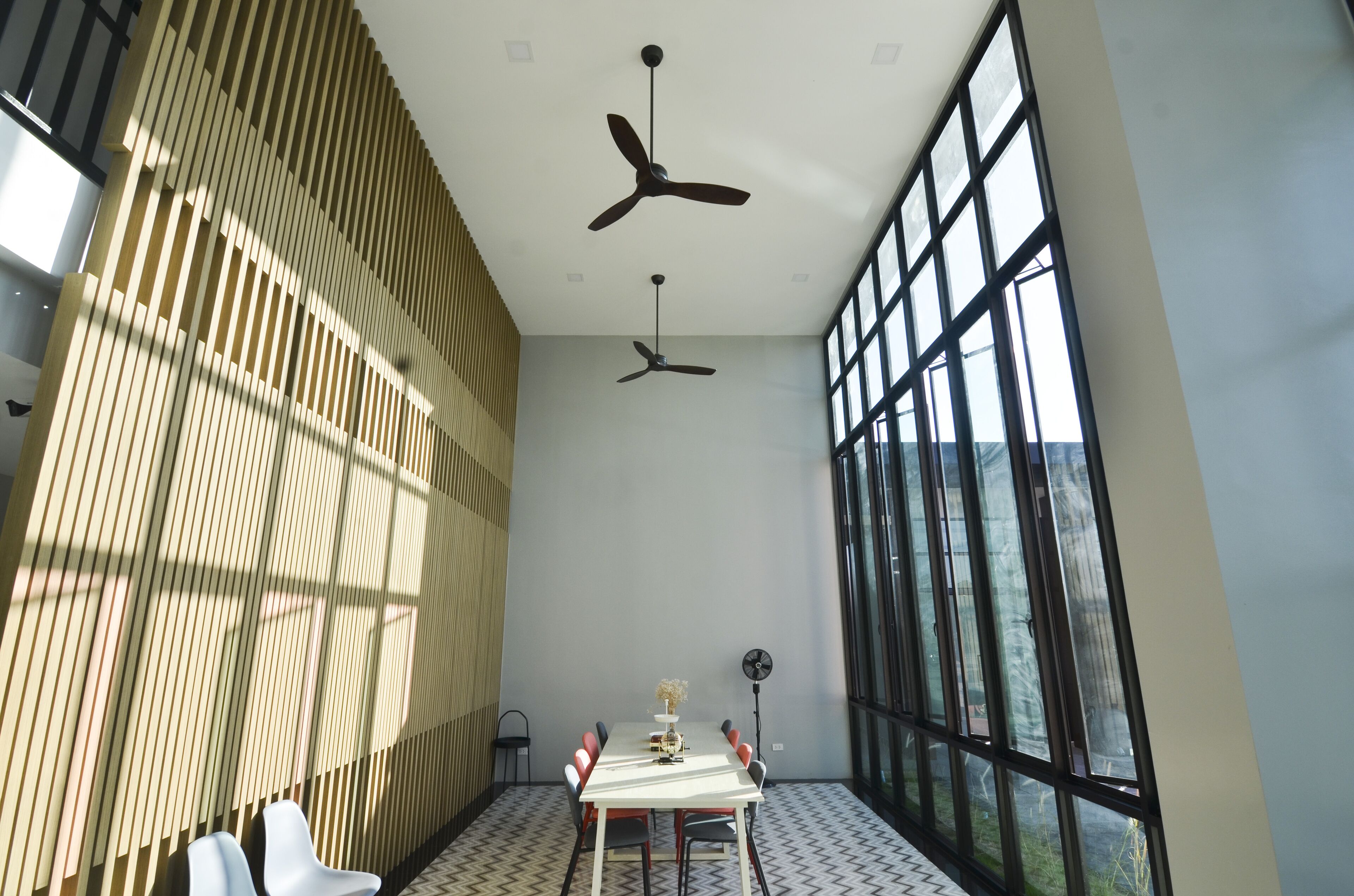 Una sala de conferencias moderna con una larga mesa, sillas, ventiladores de techo y ventanas amplias.