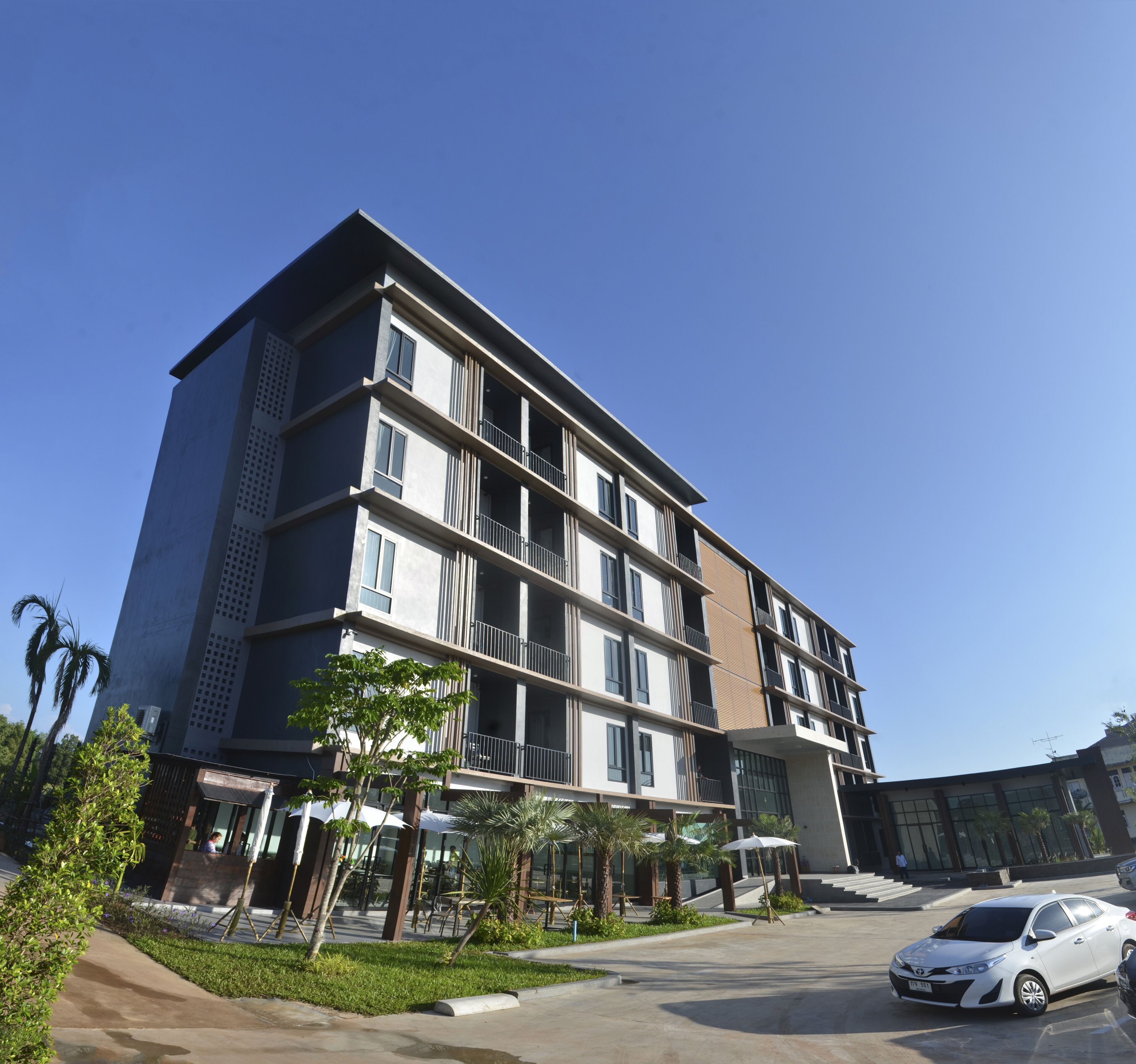 A multi-story residential building with balconies, a parking area, and a clear sky.