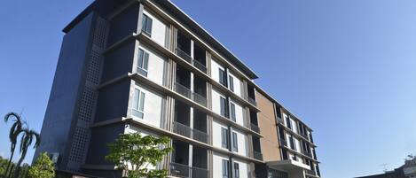 A multi-story residential building with balconies, a parking area, and a clear sky.