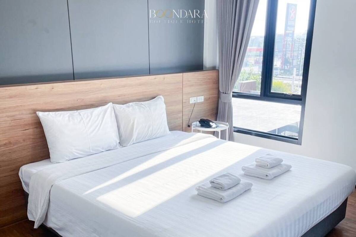 A modern hotel room with a large bed, a nightstand, and a view of the city through the window.
