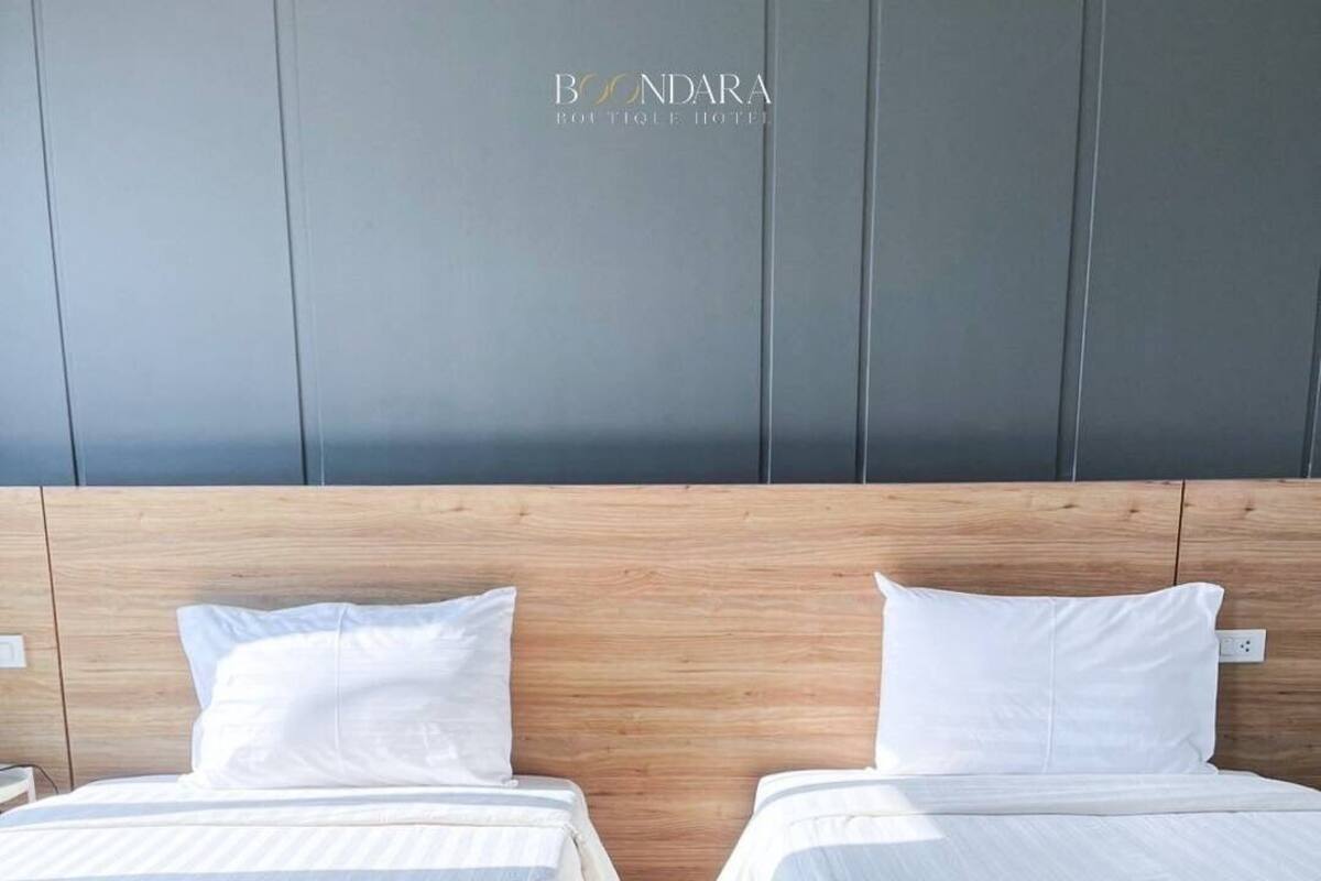 A hotel room with two beds, wooden headboards, and a grey wall.