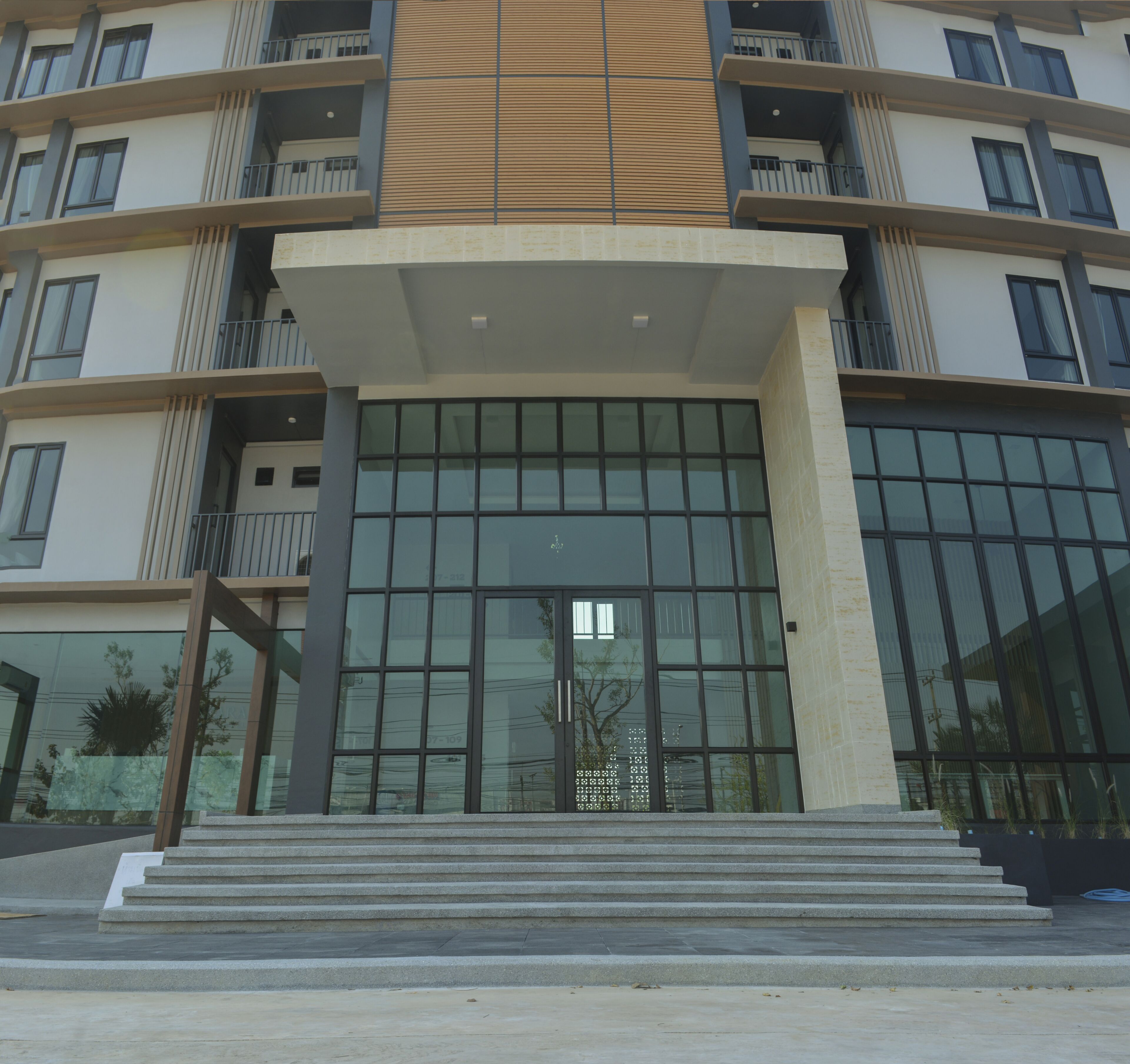 A modern building with a large glass entrance, multiple balconies, and a central entrance with steps.