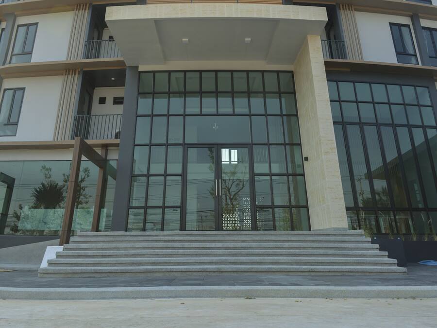 A modern building with a large glass entrance, multiple balconies, and a central entrance with steps.