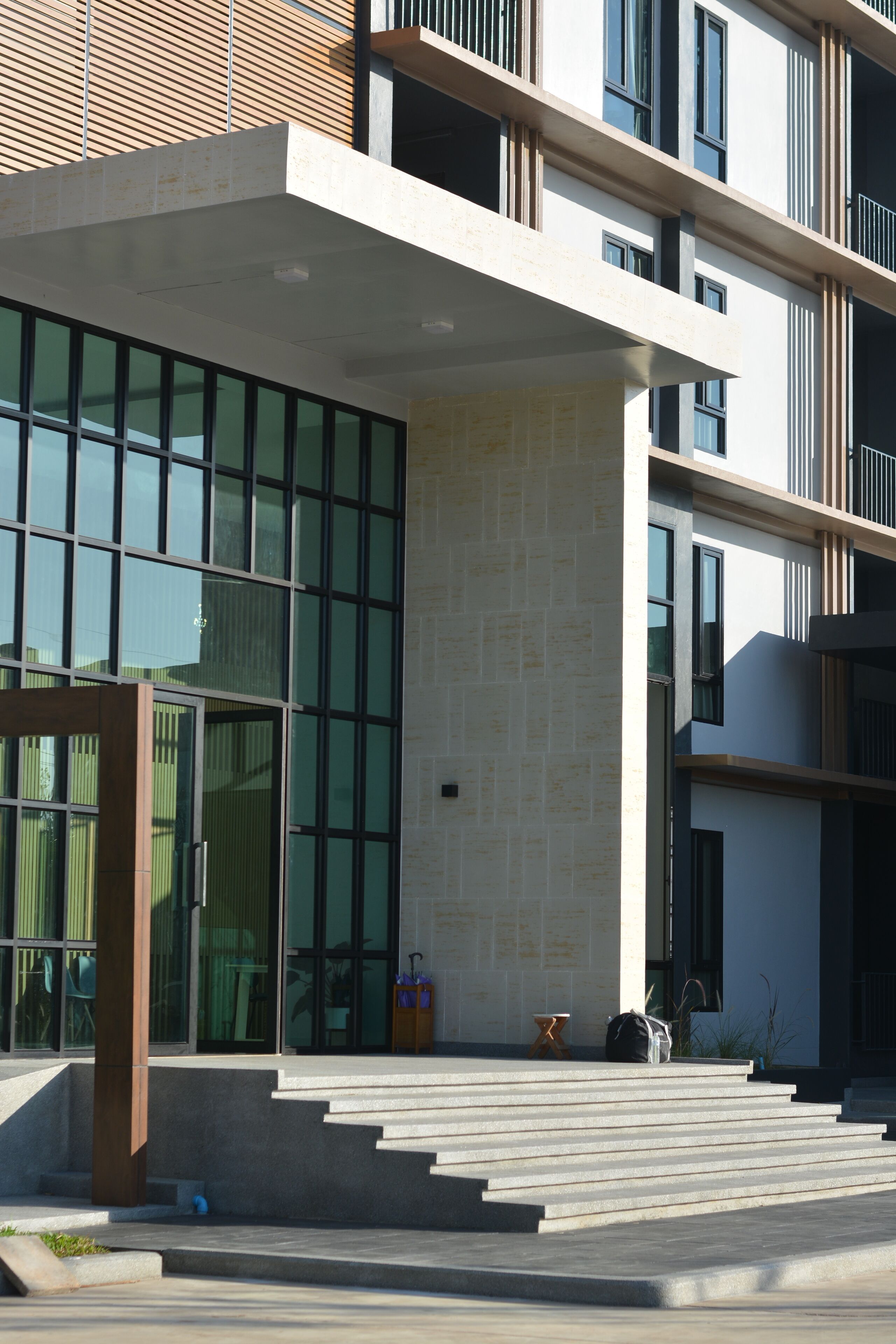 A modern building with a glass entrance, concrete steps, and a wooden facade.