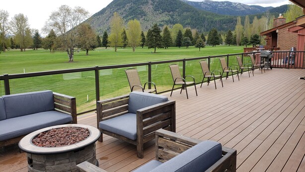 Une terrasse avec coin salon extérieur, un foyer et une vue sur un champ verdoyant et des montagnes.