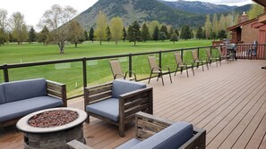 A deck with outdoor seating, a fire pit, and a view of a green field and mountains.