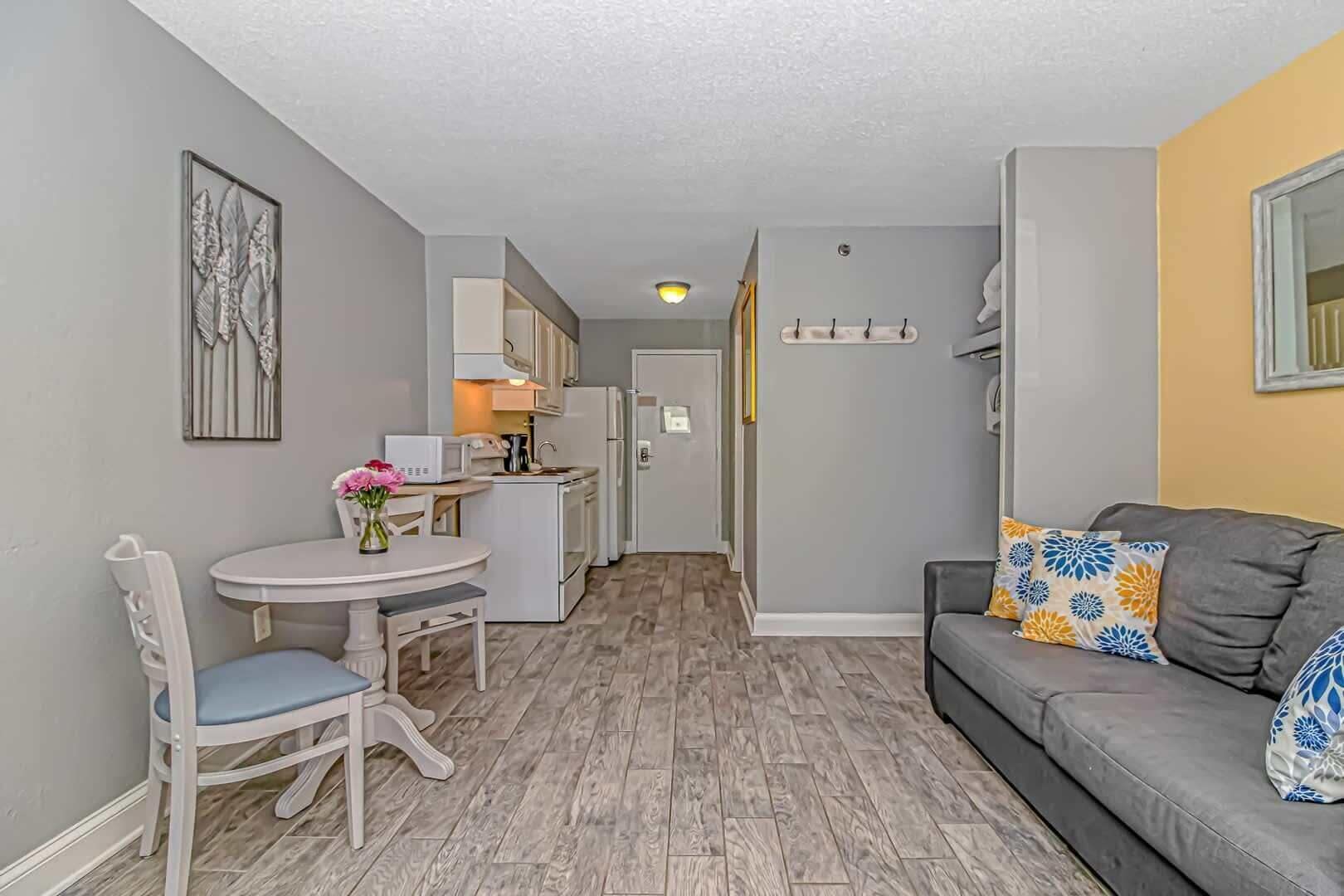 A compact living space with a kitchenette, a dining area with a table and chairs, and a sofa with patterned cushions.