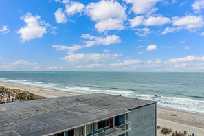 Vista a la playa desde un edificio con techo plano, balcón y cielo despejado.
