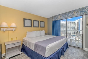 A hotel room with a bed, two wall-mounted lamps, a nightstand, a dresser, and a balcony with chairs.