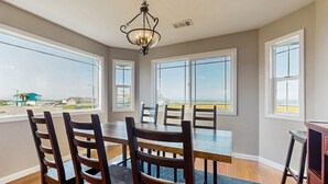 A dining area with a large table and chairs, large windows with a view of the beach, and a chandelier.