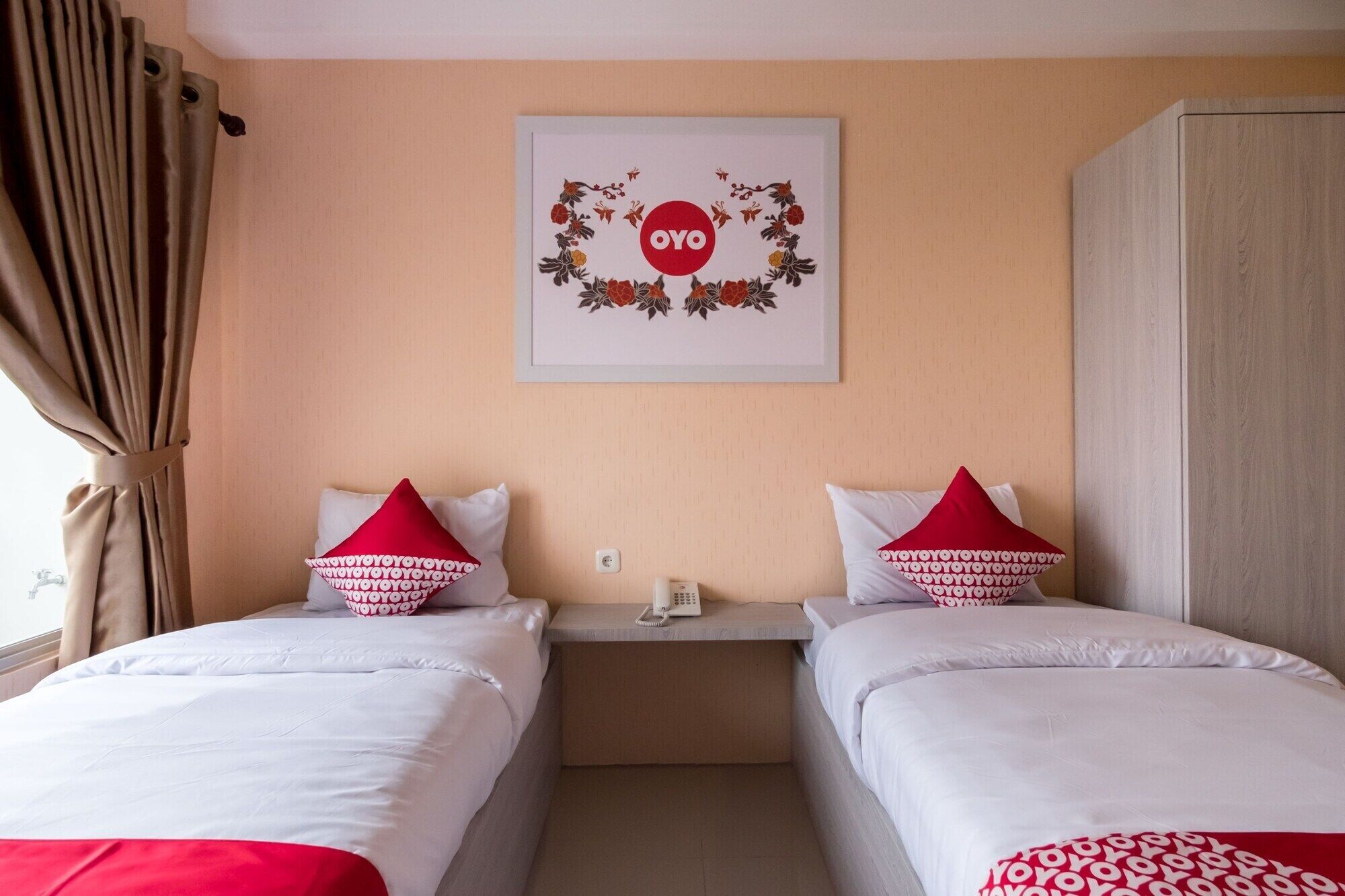 Habitación de hotel con dos camas, cada una con ropa blanca y almohadas rojas. Encima de las camas hay una obra de arte enmarcada y un teléfono en la mesita de noche.