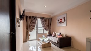 A modern living room with a sofa, a coffee table, and a TV mounted on the wall. - Skyview Setiabudi Premium (Medan)