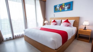 A hotel room with a large bed, two bedside tables, a window with curtains, and a colorful abstract painting on the wall.