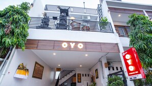 Ein modernes Gebäude mit einem auffälligen "OYO"-Schild am Eingang, einer Treppe, die zu der oberen Etage führt, und einem mit Pflanzen bepflanzten Balkon.