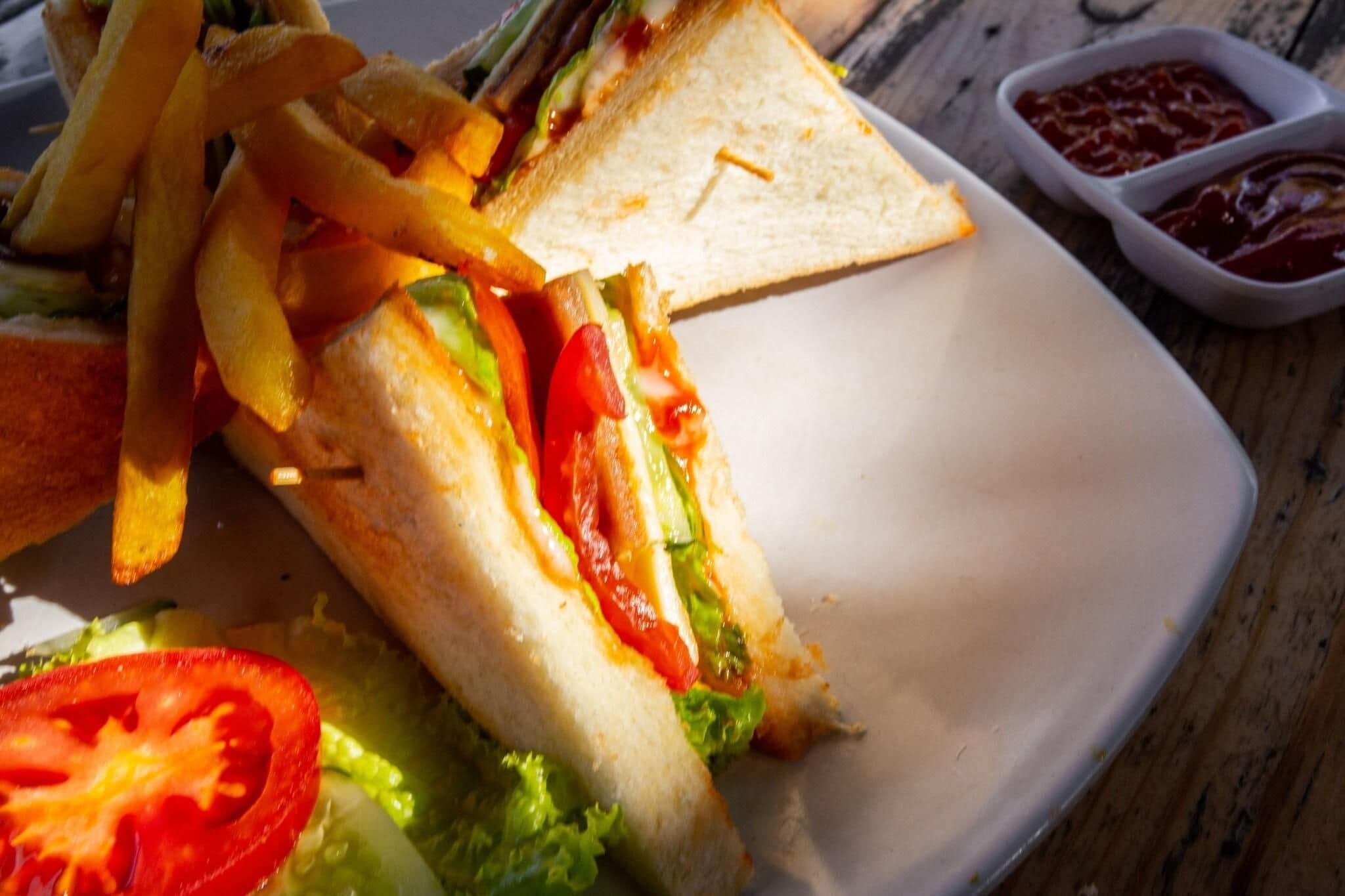 A sandwich with lettuce, tomato, and cheese, accompanied by fries and a slice of toasted bread on a plate.