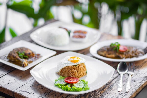 A table with various dishes, including fried rice with a fried egg, a fish dish, and a plate of rice with a side dish.