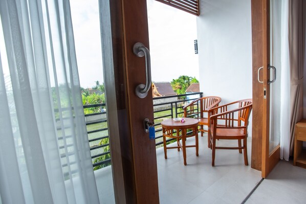 A balcony with a table and chairs, a view of greenery, and a building in the background. - OYO 1207 Pondok 789 (Munggu)