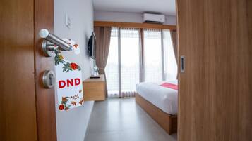 A hotel room with a bed, a wooden door, a wall-mounted TV, and a window with curtains.