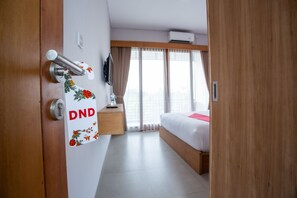 A hotel room with a bed, a wooden door, a wall-mounted TV, and a window with curtains. - OYO 1207 Pondok 789 (Munggu)