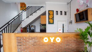 Ein Empfangsbereich mit 'OYO'-Beschriftung, eine Treppe, ein an der Wand befestigter Fernseher und ein Blumentopf.