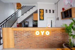Uma mesa de recepção com a sinalização 'OYO', uma escadaria, uma televisão fixada na parede e um vaso de plantas.