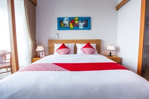 Een hotelkamer met een groot bed, twee nachtkastjes met lampen, een rode en witte gebloemde plaid, een blauw abstract schilderij aan de muur en uitzicht op het omliggende landschap.
