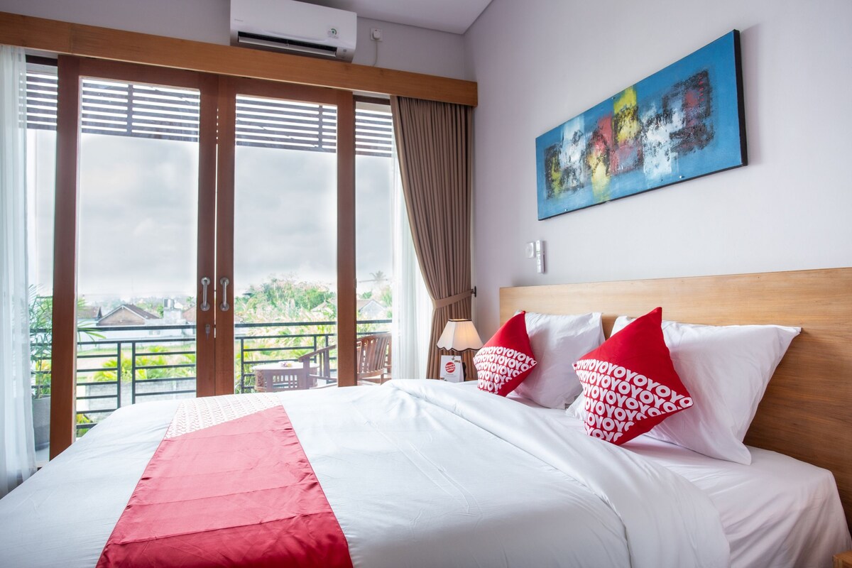 A hotel room with a bed, a painting, and a view of greenery.