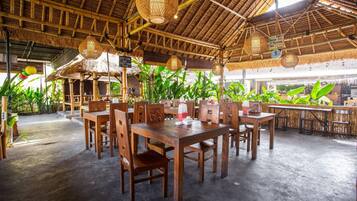 A restaurant with wooden tables and chairs, thatched roof, hanging lights, and potted plants.