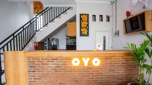 A reception desk with 'OYO' signage, a staircase, a wall-mounted TV, and a potted plant.