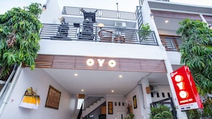 A modern building with a prominent "OYO" sign at the entrance, a staircase leading to the upper floor, and a balcony with plants.