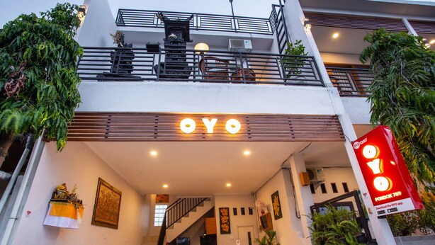 Ein Hotelzugang mit einem gut sichtbaren 'OYO'-Schild, einer Treppe, die zu den oberen Stockwerken führt, und Blumentöpfen vor dem Eingang.