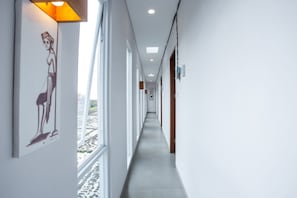 A long, narrow hallway with white walls and a grey floor, featuring a large window on the left and a door on the right. - OYO 1207 Pondok 789 (Munggu)