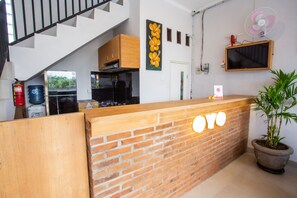 A reception area with a brick counter, a wooden cabinet, a mounted TV, and a potted plant. - OYO 1207 Pondok 789 (Munggu)