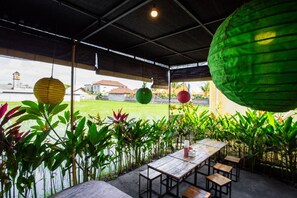 Een terras met tafels en stoelen, omringd door weelderige begroeiing en decoratieve lantaarns.