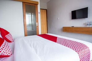 A hotel room with a bed, red and white bedding, a TV, and a water dispenser.