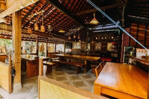 Ein Restaurant mit Holztischen und -bänken, gefliestem Boden und einer hohen Decke mit freiliegenden Balken und Pendelleuchten.