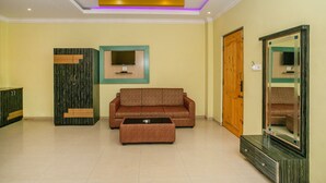 A room with a sofa, a coffee table, a TV, a wardrobe, and a mirror. - OYO 436 Emirates Suites (Bengaluru)