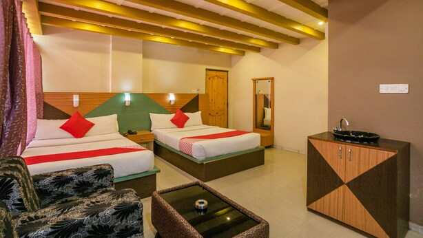 A hotel room with two beds, a sofa, a coffee table, and a cabinet. - OYO 436 Emirates Suites (Bengaluru)
