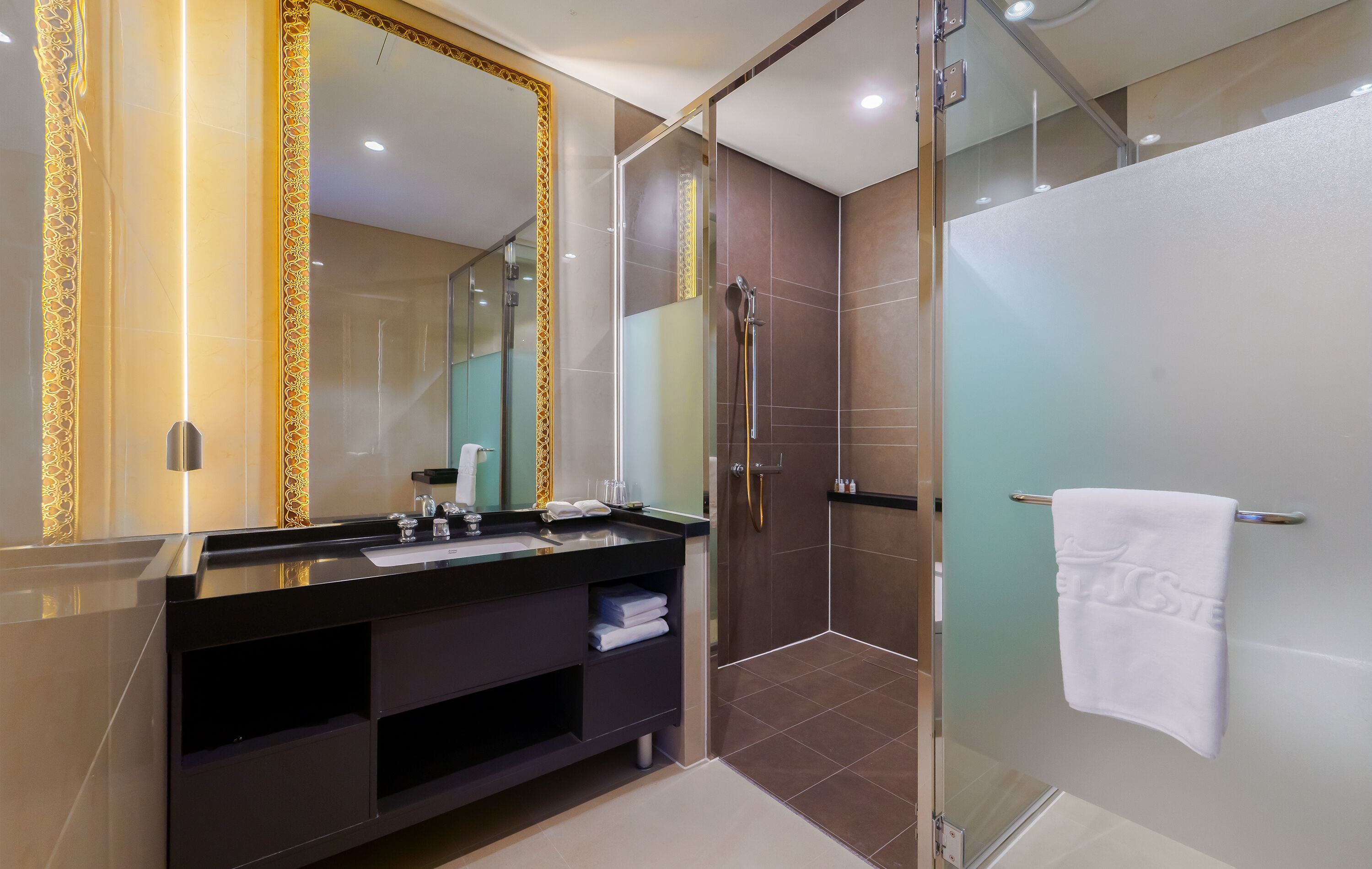 Un baño moderno con un espejo grande, tocador oscuro y ducha con cerramiento de vidrio.