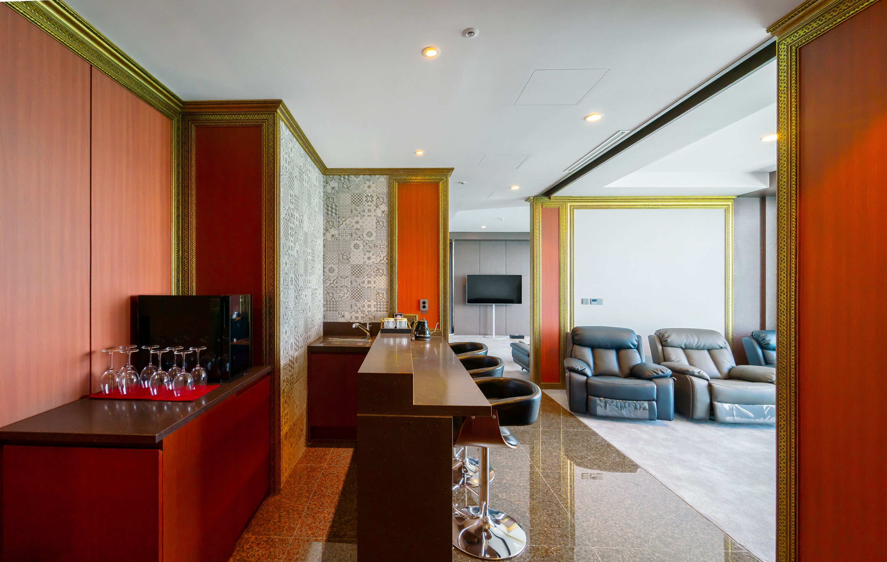 A modern hotel room with a bar area, seating, and a television.