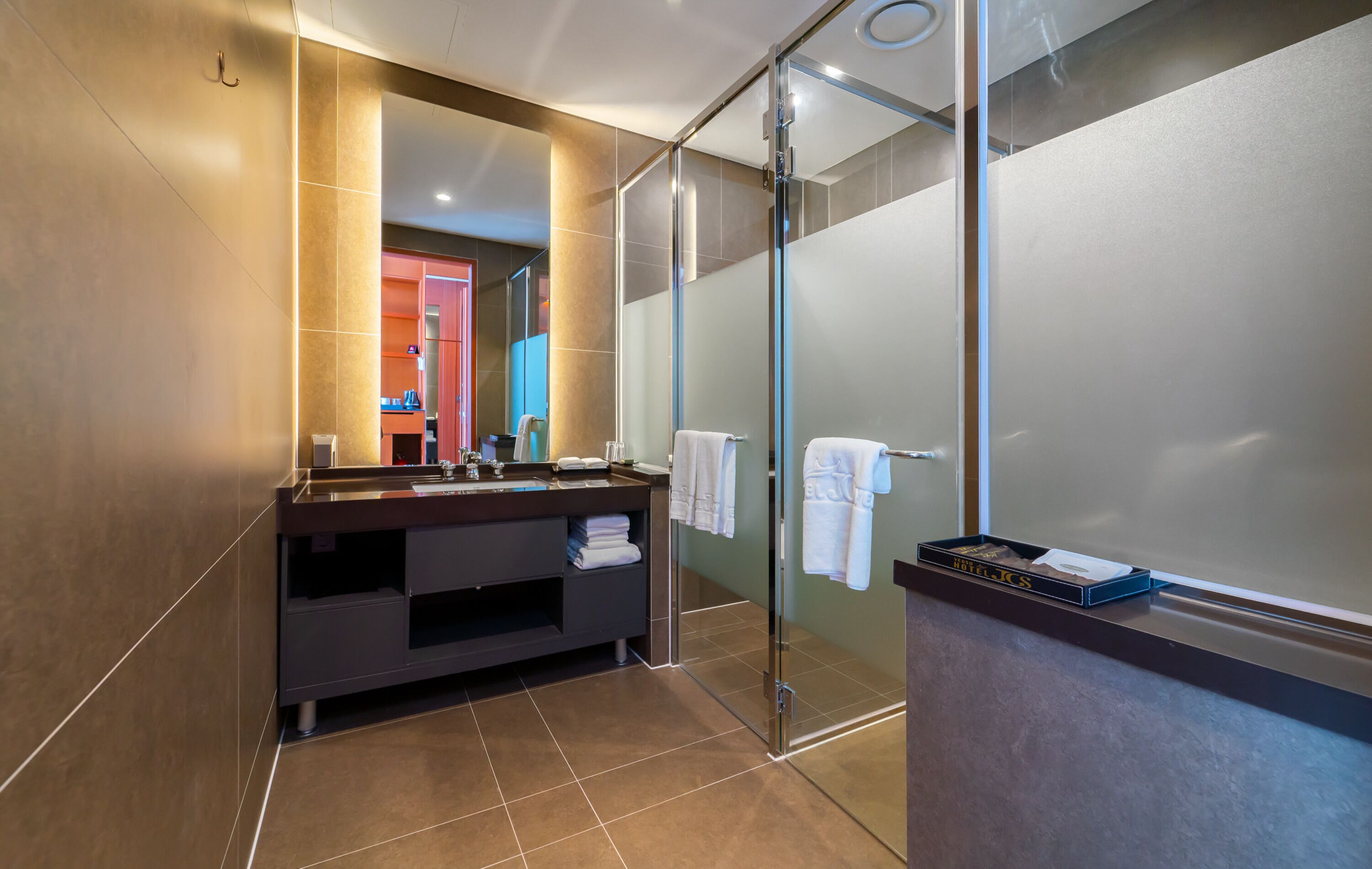 A modern bathroom with a glass shower enclosure, a dark vanity, and a large mirror.