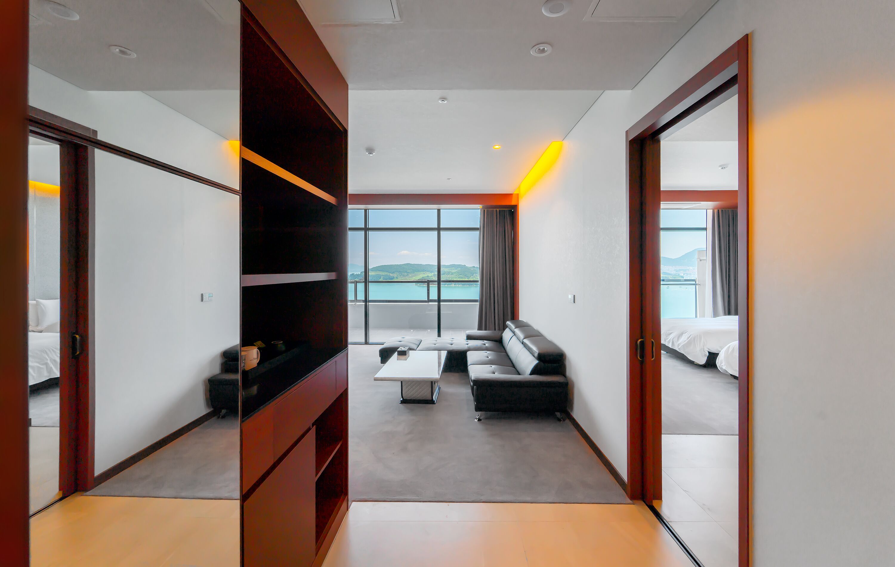 A modern hotel room with a large window, a sofa, a coffee table, and a wardrobe.