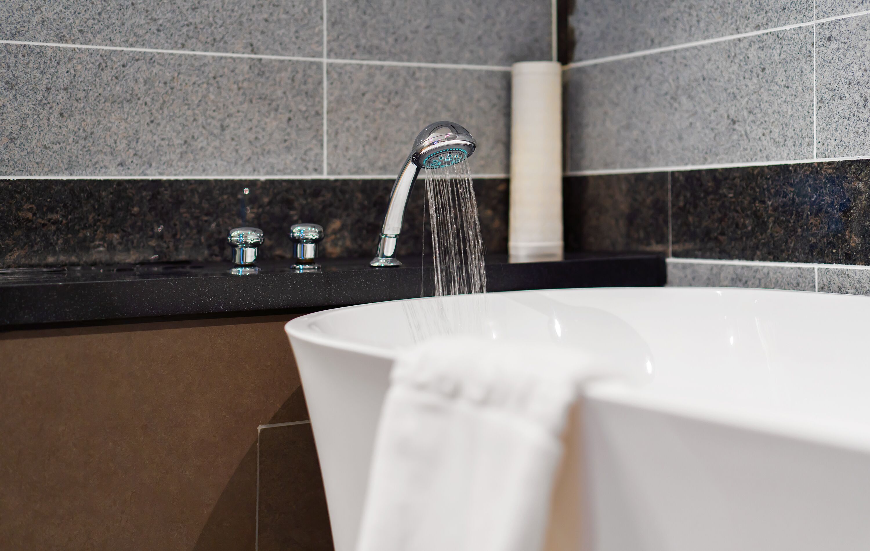 A modern bathroom with a freestanding bathtub, a handheld showerhead, and a towel hanging on the side.