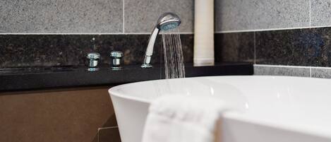 A modern bathroom with a freestanding bathtub, a handheld showerhead, and a towel hanging on the side.