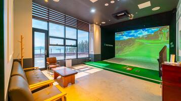 A modern room with a large screen displaying a golf game, a seating area with a sofa and chairs, and a view of the outdoors through large windows.