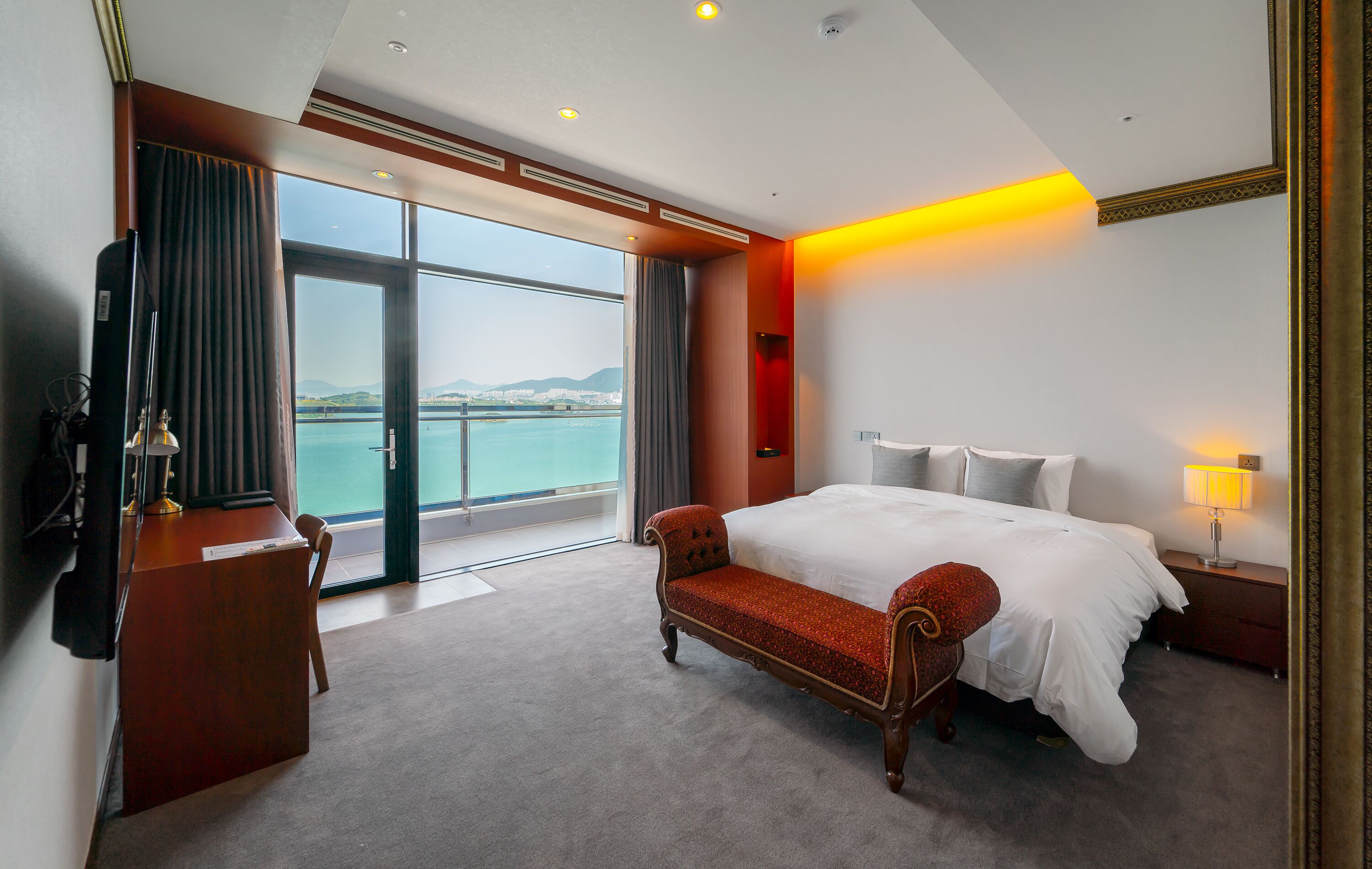 Quarto de hotel com cama grande, escrivaninha, cadeira, televisão e vista para o mar.