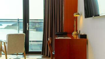 A hotel room with a desk, chair, and a view of the ocean through a large window.