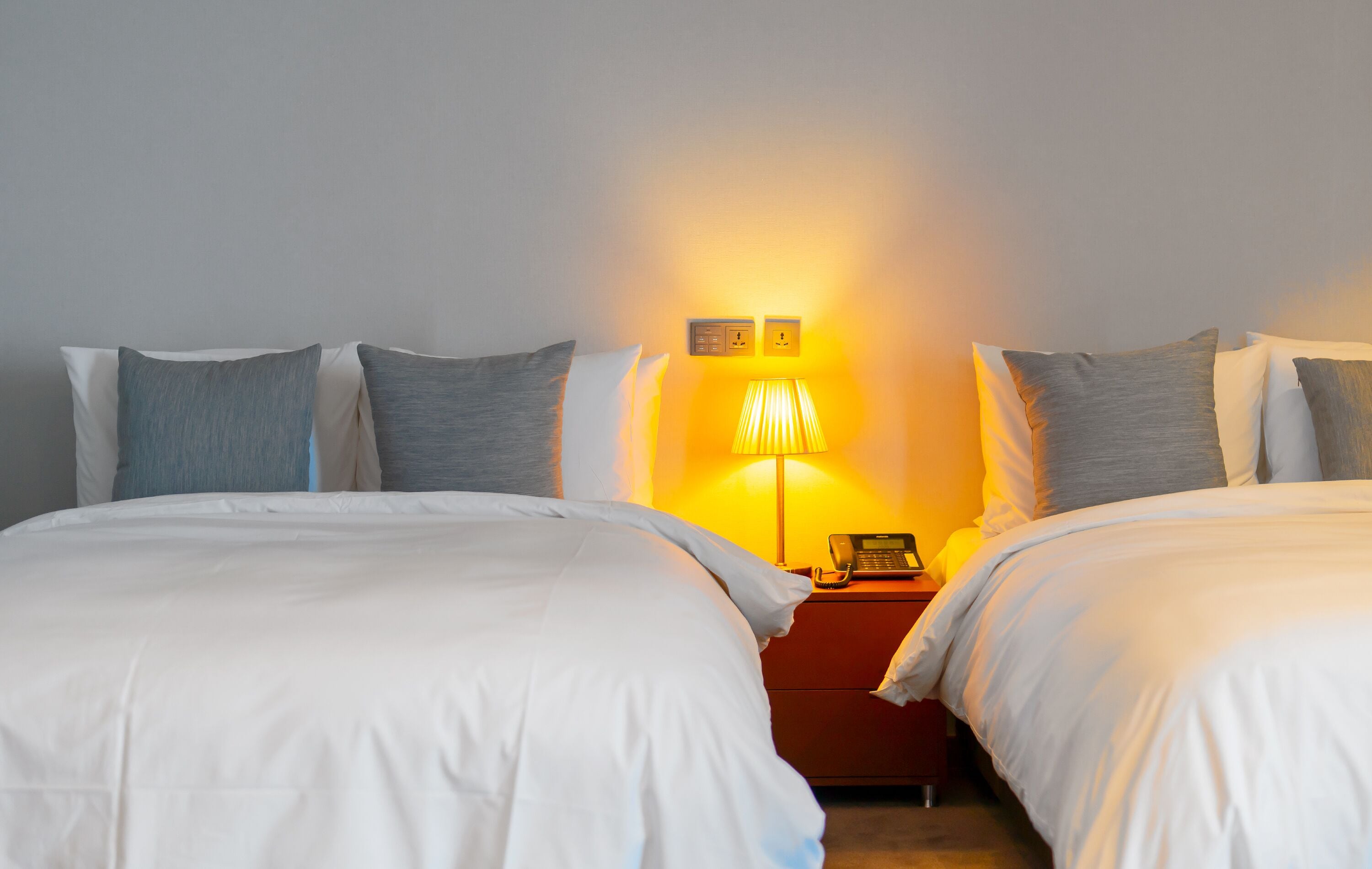 A hotel room with two beds, a nightstand with a lamp, and a phone.